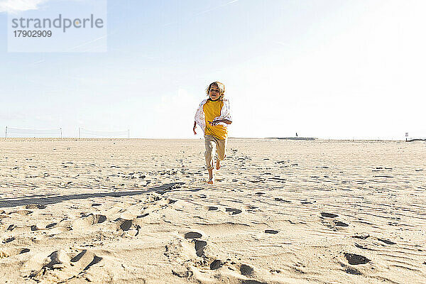 Verspielter Junge läuft an sonnigem Tag am Strand