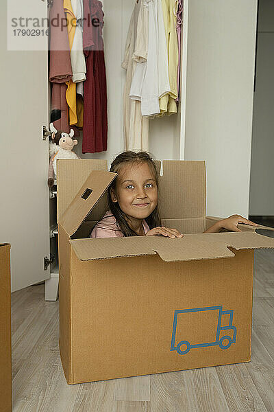 Lächelndes Mädchen sitzt zu Hause im Karton