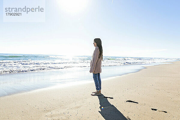 Mädchen blickt an einem sonnigen Tag vom Strand aus auf den Horizont