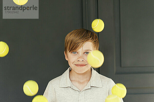 Lächelnder Junge mit fallenden Tennisbällen zu Hause