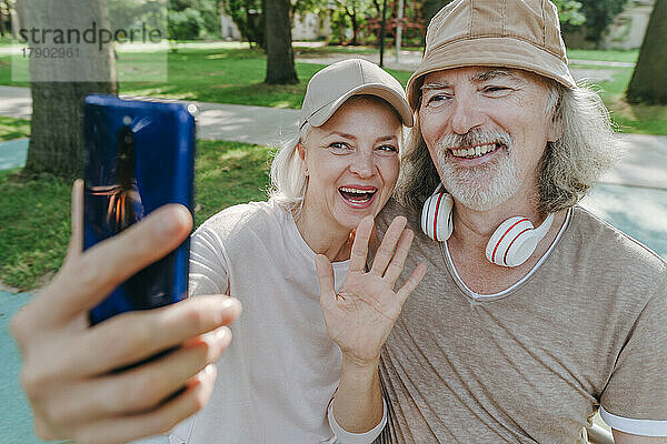 Glückliches Paar  das im Park per Videoanruf über sein Smartphone spricht