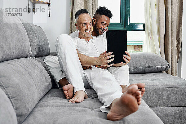 Reifer Mann benutzt Tablet-PC und sitzt mit seinem Freund zu Hause auf dem Sofa