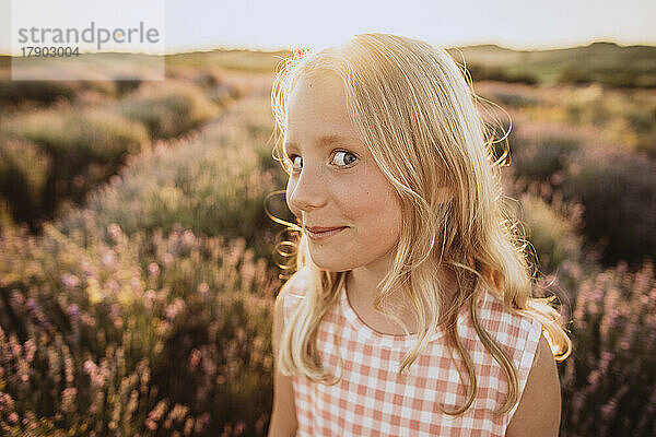 Mädchen mit blonden Haaren macht Gesichtsausdruck im Lavendelfeld bei Sonnenuntergang