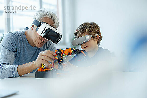 Älterer Mann und Enkel mit futuristischer Brille beobachten Robotermodell zu Hause