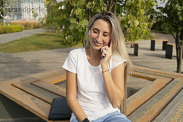 Glückliche junge Frau  die im Park mit ihrem Smartphone spricht