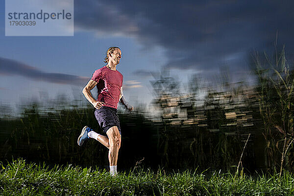 Smiling sportsman running on grass at dusk
