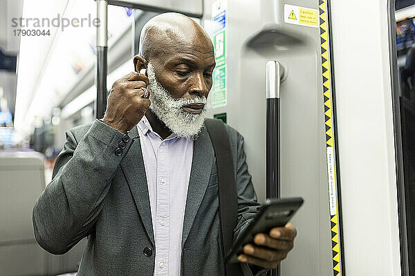 Leitender Geschäftsmann nutzt Smartphone und stellt kabellose In-Ear-Kopfhörer im Zug ein