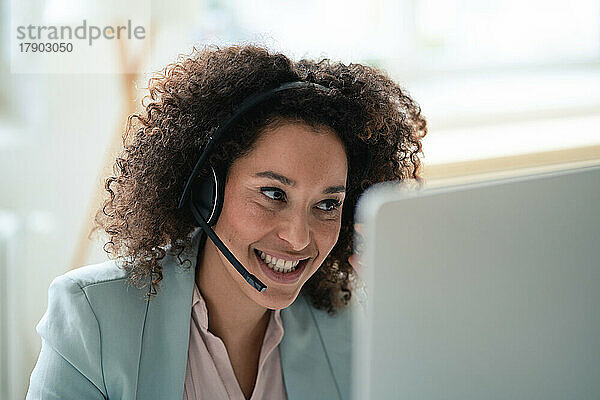 Lächelnder Kundendienstmitarbeiter mit Headset am Arbeitsplatz