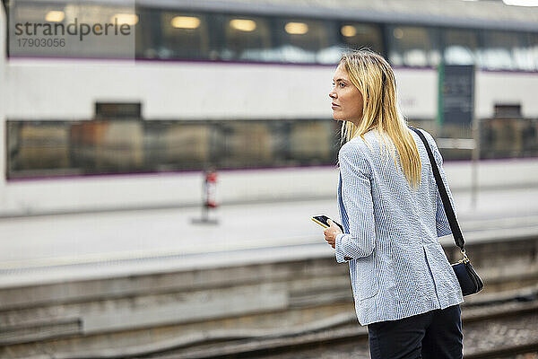 Geschäftsfrau mit blonden Haaren wartet am Bahnhof auf den Zug