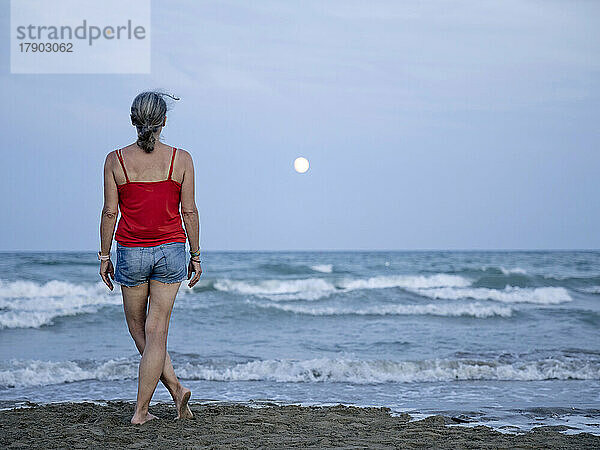 Frau schaut vom Strand aus auf den Mond