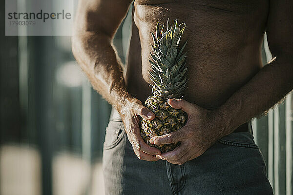 Mit nacktem Oberkörper reifer Mann hält Ananas