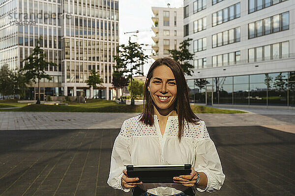 Glückliche Geschäftsfrau hält Tablet-PC im Büropark