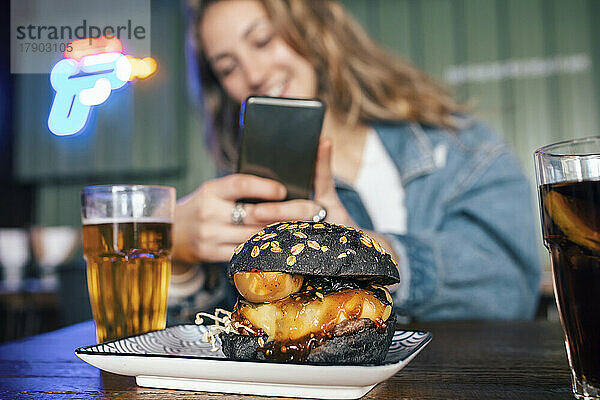 Junge Frau fotografiert Burger per Smartphone im Restaurant