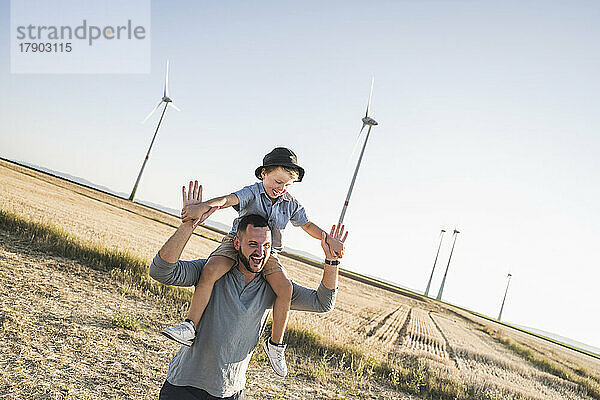 Vater trägt Sohn auf Schultern vor Windkraftanlagen