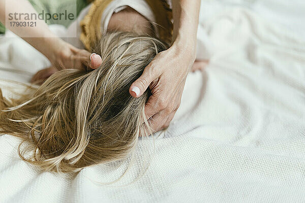 Mother tying daughter's hair lying on bed