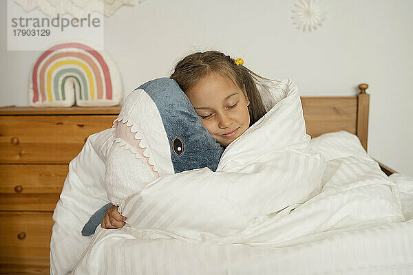 Mädchen schläft mit einem unter einer weißen Decke eingewickelten Spielzeughai im Kinderzimmer
