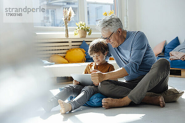 Älterer Mann nutzt Tablet-PC mit Enkel im Wohnzimmer