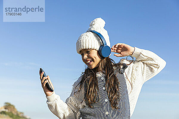 Mädchen benutzt Smartphone und hört Musik mit Kopfhörern und genießt den sonnigen Tag
