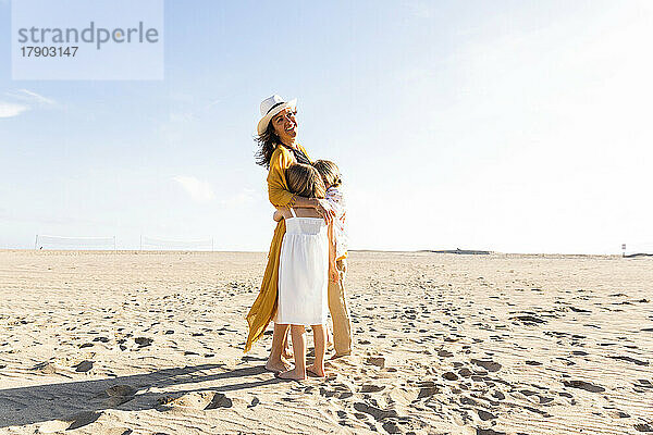 Glückliche reife Frau umarmt Sohn und Tochter an einem sonnigen Tag am Strand