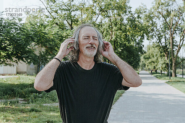 Lächelnder älterer Mann mit Kopfhörern  der im Park Musik genießt