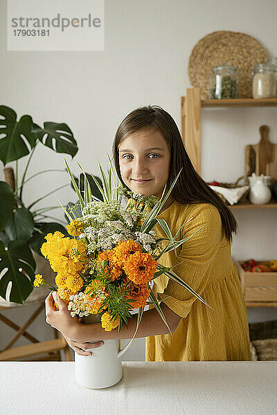 Lächelndes Mädchen umarmt Blumenvase am Tisch in der Küche