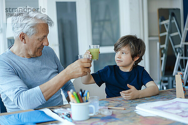 Junge toastet Saft mit Großvater am Tisch zu Hause