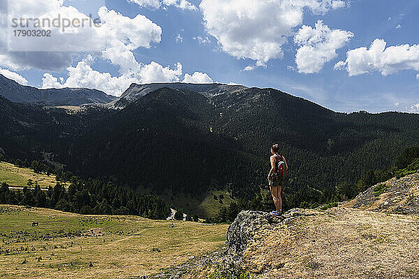 Junge Frau mit Rucksack steht an einem sonnigen Tag vor dem Berg