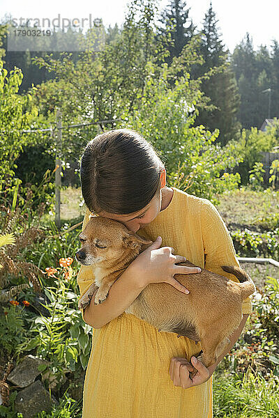 Girl embracing dog in garden on sunny day