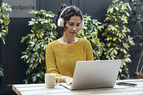 Geschäftsfrau hört Musik über Kopfhörer und arbeitet am Laptop im Café