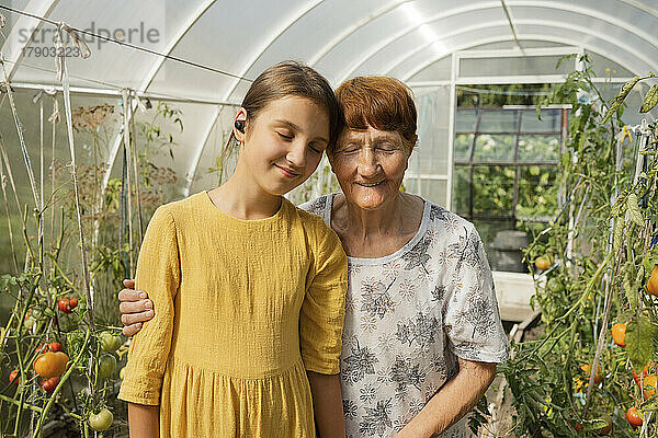 Lächelnde Großmutter und Enkelin stehen zusammen mit geschlossenen Augen im Gewächshaus