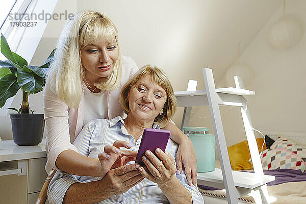 Lächelnde blonde Frau bringt ihrer Mutter zu Hause das Smartphone bei