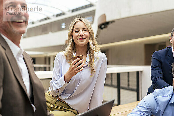Lächelnde Geschäftsfrau beim Kaffeetrinken mit Kollegen im Büro