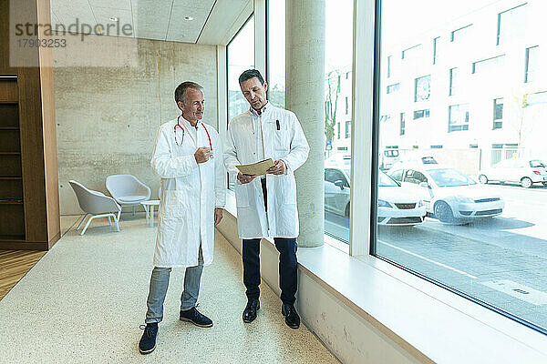 Ärzte in Laborkitteln diskutieren über Krankenakten  die am Fenster des Krankenhauses stehen