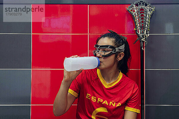 Junge Frau mit Schutzbrille trinkt Wasser in der Umkleidekabine