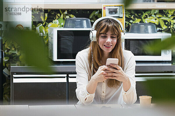 Lächelnde Geschäftsfrau mit Kopfhörern  die in der Cafeteria über ihr Smartphone im Internet surft