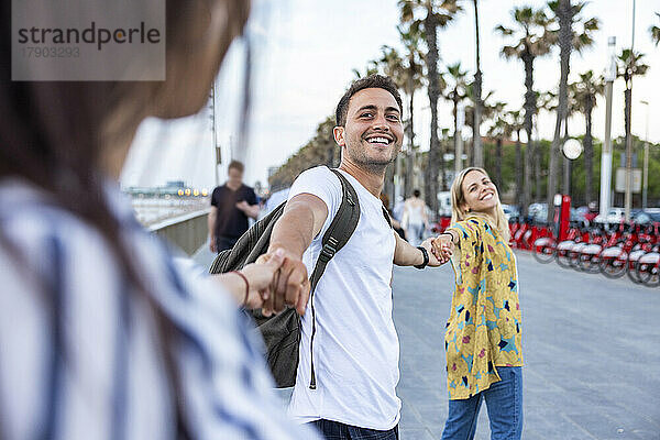 Fröhliche junge Männer und Frauen halten sich gegenseitig an den Händen und genießen die Promenade