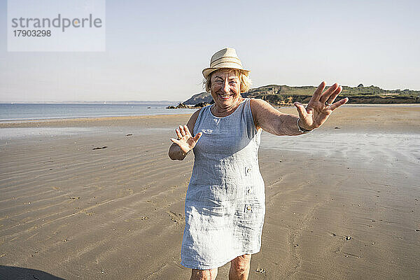 Fröhliche Seniorin tanzt und hat im Urlaub Spaß am Strand