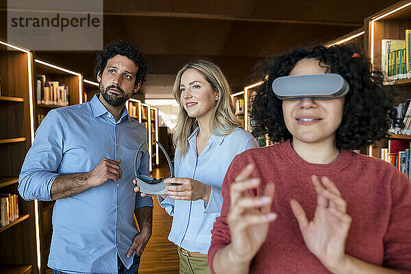 Gemischtrassige Kollegen mit VR-Brille in beleuchteter Bibliothek