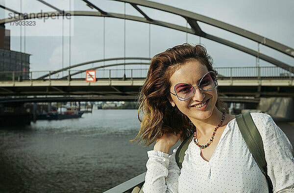 Glückliche Frau mit Brille steht an einem sonnigen Tag vor der Brücke  Hamburg  Deutschland