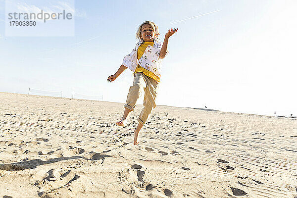 Verspielter Junge springt an sonnigem Tag am Strand