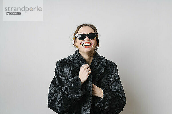 Happy woman with sunglasses wearing fur jacket over white background