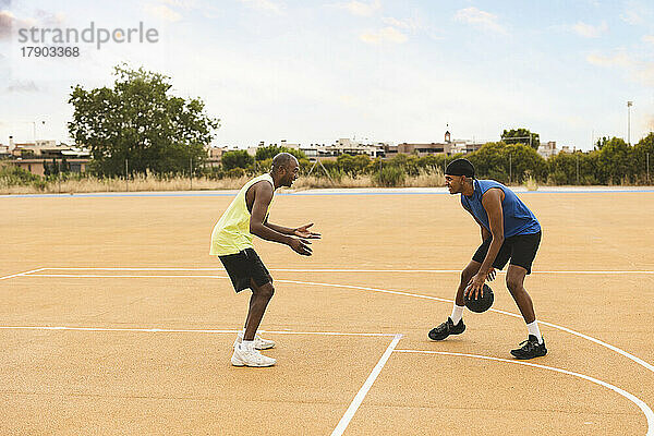 Sohn dribbelt Basketball und spielt mit Vater auf dem Sportplatz