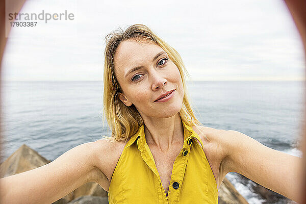 Schöne blonde Frau  die ein Selfie vor dem Meer macht