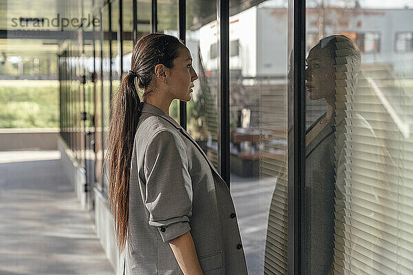 Geschäftsfrau mit langen Haaren blickt auf die Spiegelung an der Glaswand