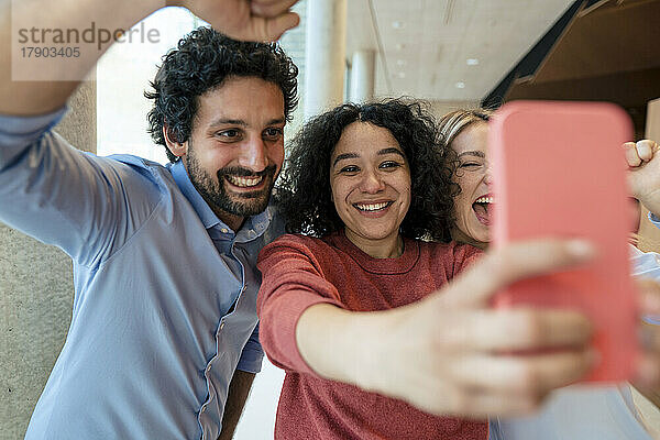 Cheerful woman taking selfie with colleagues on mobile phone
