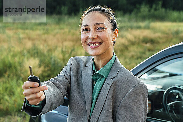 Glückliche schöne Verkäuferin mit Schlüssel  die vor dem Auto steht