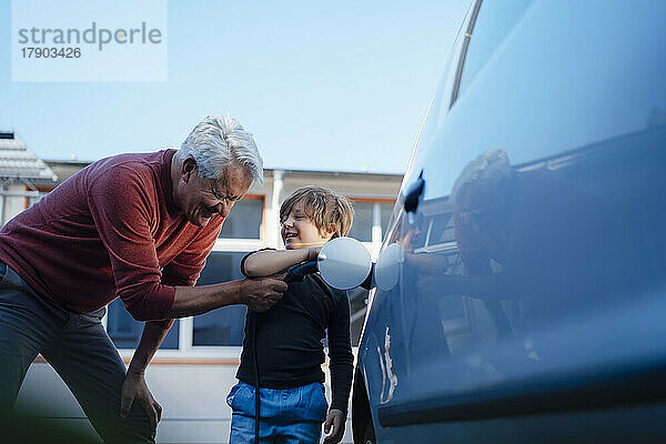Glücklicher älterer Mann und Enkel laden Elektroauto auf