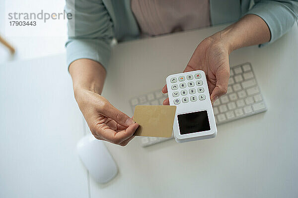 Geschäftsfrau hält Kreditkarte und Lesegerät am Schreibtisch im Büro
