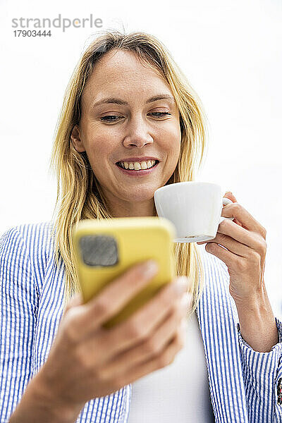 Glückliche Geschäftsfrau hält Kaffee mit Smartphone