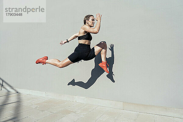 Junge Frau sprintet an sonnigem Tag an der Mauer entlang